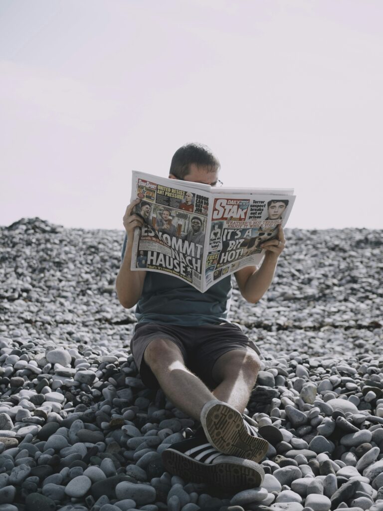 pexels-photo-18299830-18299830 Man Reading Newspaper at Stony Beach